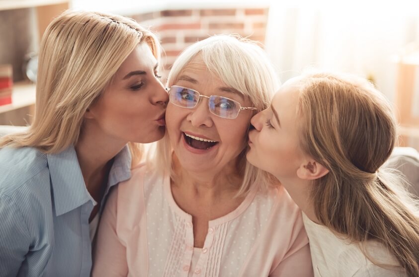 grandmother is being kissed by her daughter and granddaughter